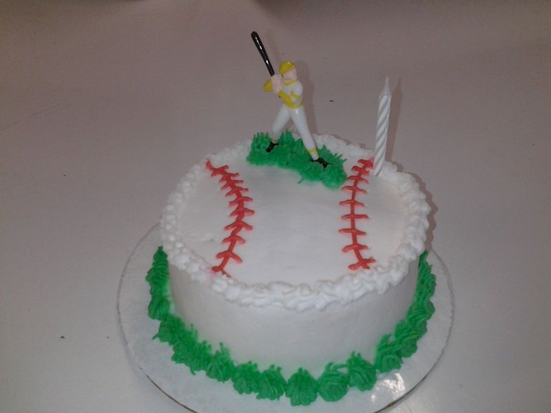 Baseball-themed birthday cake with green frosting and a batter figurine, with a lit candle.