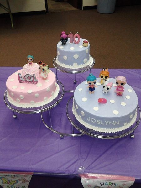 Three-tiered birthday cake display with LOL doll toppers; pink and purple frosting, white polka dots, and 