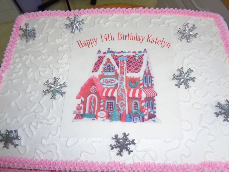 Birthday cake with a gingerbread house design, pink frosting, and snowflake decorations.