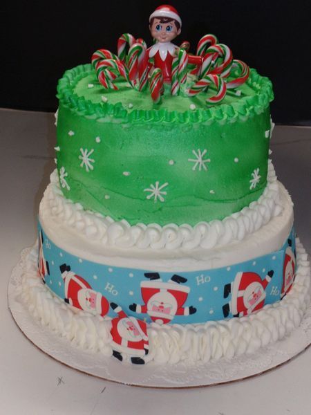 Two-tiered Christmas cake decorated with Santa figures, snowflakes, and candy canes; topped with an elf.