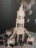 Wedding cake, multi-tiered white tower, with side cakes on a table, balloons in background.