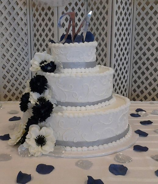 Three-tiered white cake with silver ribbon and dark and white flowers; 