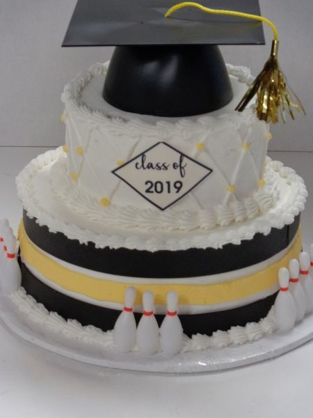 Two-tiered graduation cake with bowling pins, black and yellow stripes, mortarboard topper, and 