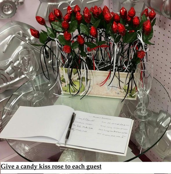 Candy kiss roses in a box on a table next to a guest book and champagne glasses.