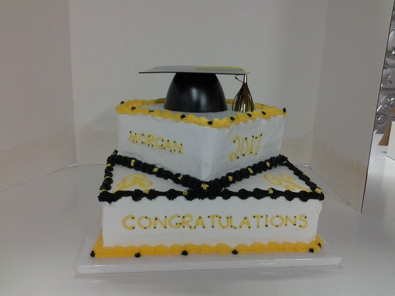 Two-tiered graduation cake with black and yellow frosting, topped with a mortarboard cap; 