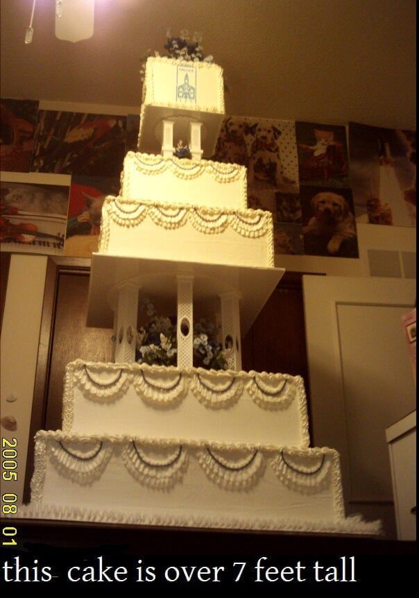 Tall, multi-tiered white cake with decorative frosting, on a stand.  Cake reaches above eye level.