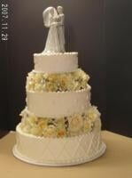 Four-tiered white wedding cake with floral accents and bride/groom figurine on top.