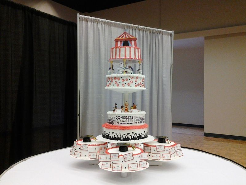 Circus-themed tiered cake with carousel top, set on a table with individual cakes around the base.