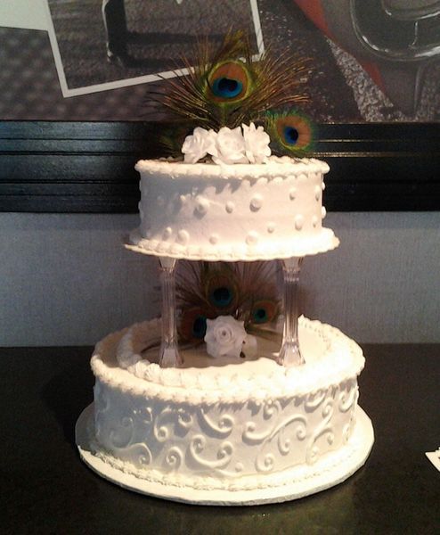 Two-tiered white wedding cake with peacock feathers and floral decorations.
