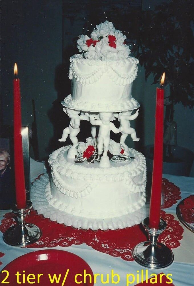 Three-tiered white wedding cake with cherub pillars, red candles.