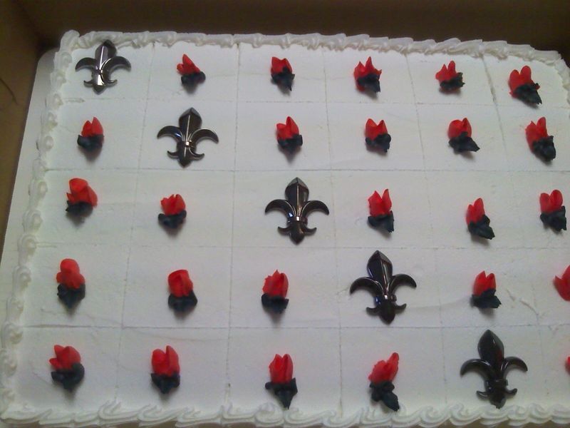Rectangular cake with white frosting, decorated with fleur-de-lis and red buttercream flames.