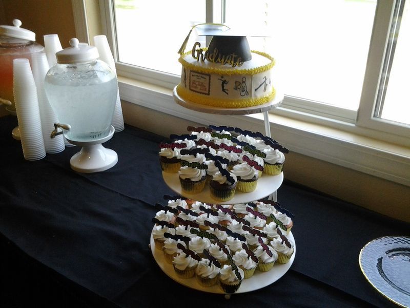 Cake and cupcakes on a table with a drink dispenser.