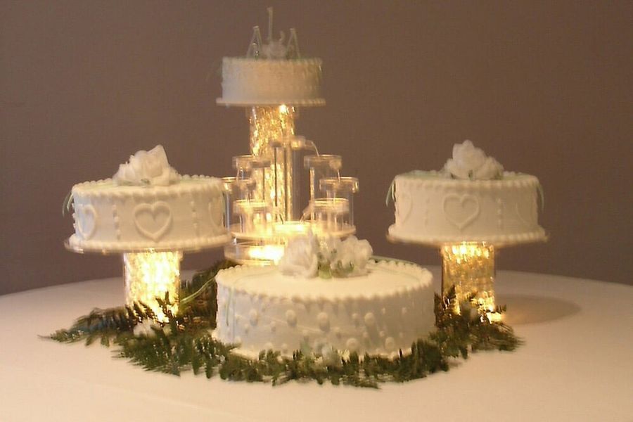 Wedding cakes on illuminated stands; fountain centerpiece with small cake, greenery.