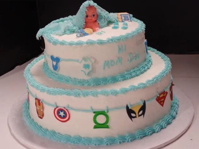 Two-tiered baby shower cake with blue frosting, a baby figurine, and superhero symbols.