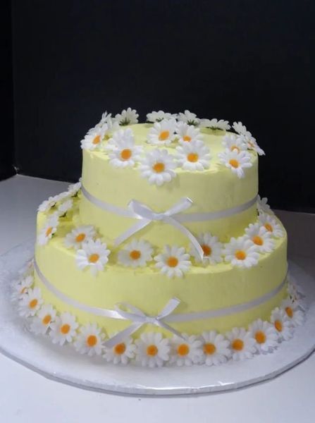 Two-tier yellow cake decorated with white daisies and ribbon.
