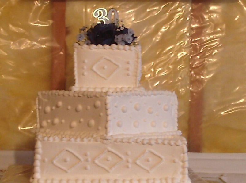 Three-tiered white cake with diamond and dot patterns, topped with flowers and a 