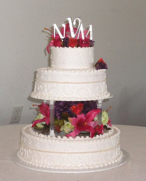 Three-tiered white wedding cake decorated with flowers and initials on top.