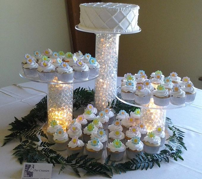 Cake and cupcakes on a tiered display with a white tablecloth, decorated with greenery and flowers.