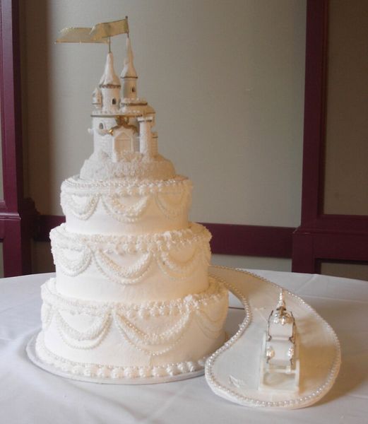 Three-tiered white wedding cake with castle topper and sugar-paste path.