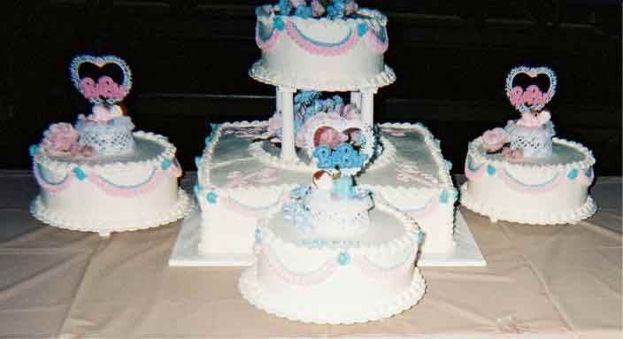 Wedding cake display: tiered white cakes with pink and blue frosting, heart toppers.