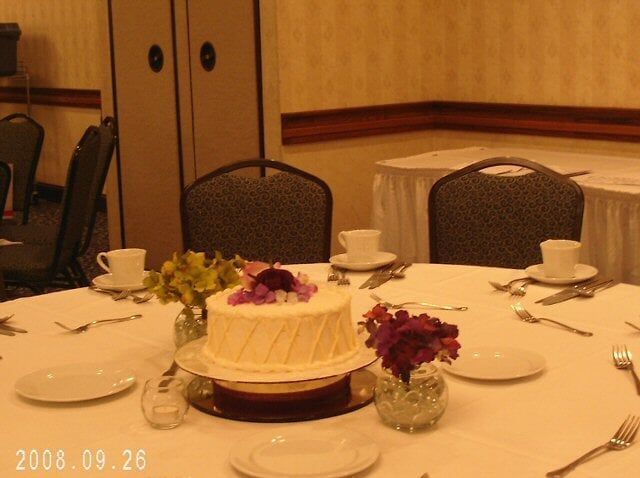 Round table set for a special event with a cake, flowers, and place settings.