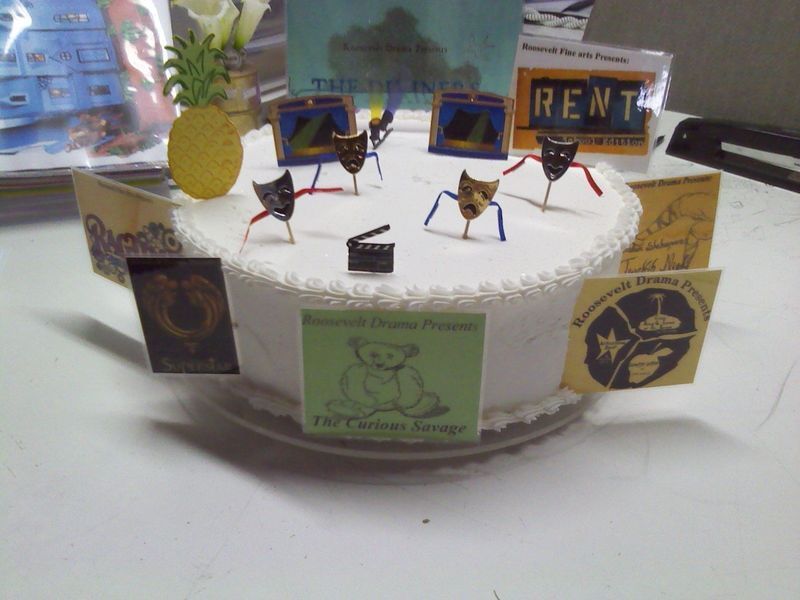 Cake decorated with drama-themed elements, including theater masks, signs, and a pineapple.