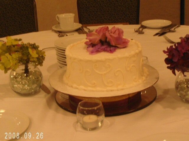 Cake centerpiece on a table, with flowers, plates, and a candle in a decorated room.