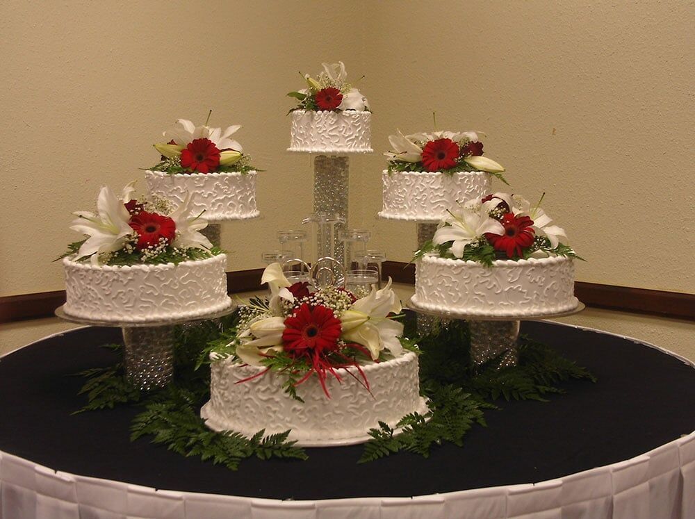 Wedding cake display: six tiers of white cakes with red flowers and lilies on a black table.