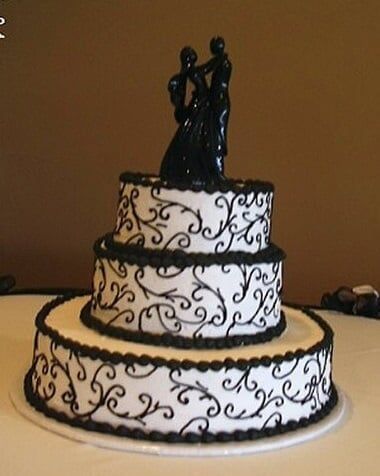 Three-tiered wedding cake, white frosting with black scrollwork, black couple topper.