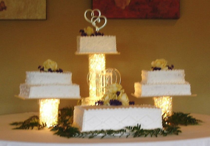 Wedding cake display with four tiers, lit up, decorated with flowers.