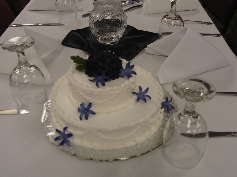 Two-tiered white frosted cake with blue flower decorations on a table set for a formal event.