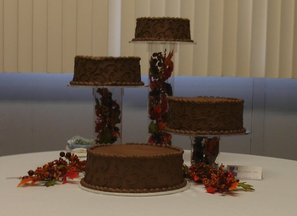 Chocolate cakes on tiered stands, decorated with fall foliage, on a white tablecloth.