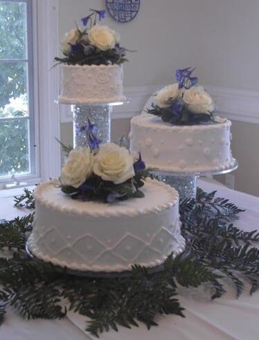 Three-tiered wedding cakes with white frosting, decorated with flowers, on a table near a window.