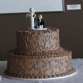 Two-tiered chocolate wedding cake with scrollwork, topped with bride and groom figurines.