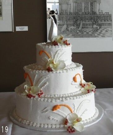 Three-tier white wedding cake with floral decorations and a topper, on a table.