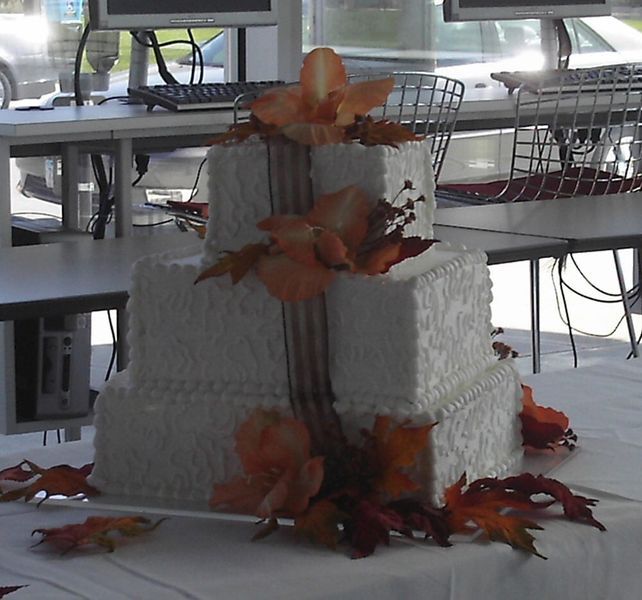 Three-tiered square wedding cake decorated with orange flowers and fall leaves.