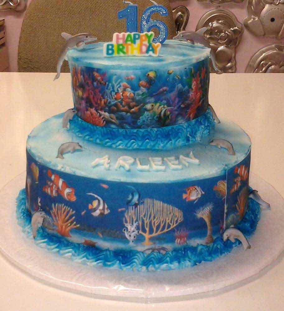 Two-tiered cake with an ocean theme. Dolphins, fish, and coral decorations. Happy 16th birthday.