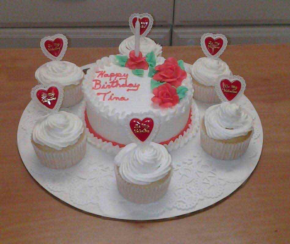 Birthday cake and cupcakes, white frosting, red roses, heart toppers, on a white doily, 