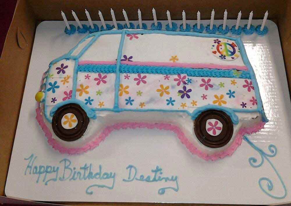 Birthday cake shaped like a flower-covered van with candles, writing 