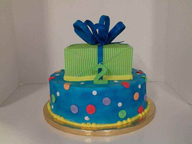 Two-tiered birthday cake, blue with polka dots, green gift-shaped top, blue bow, number 