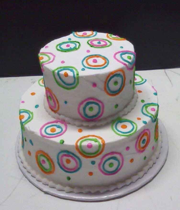 Two-tiered white cake decorated with colorful concentric circles and dots.