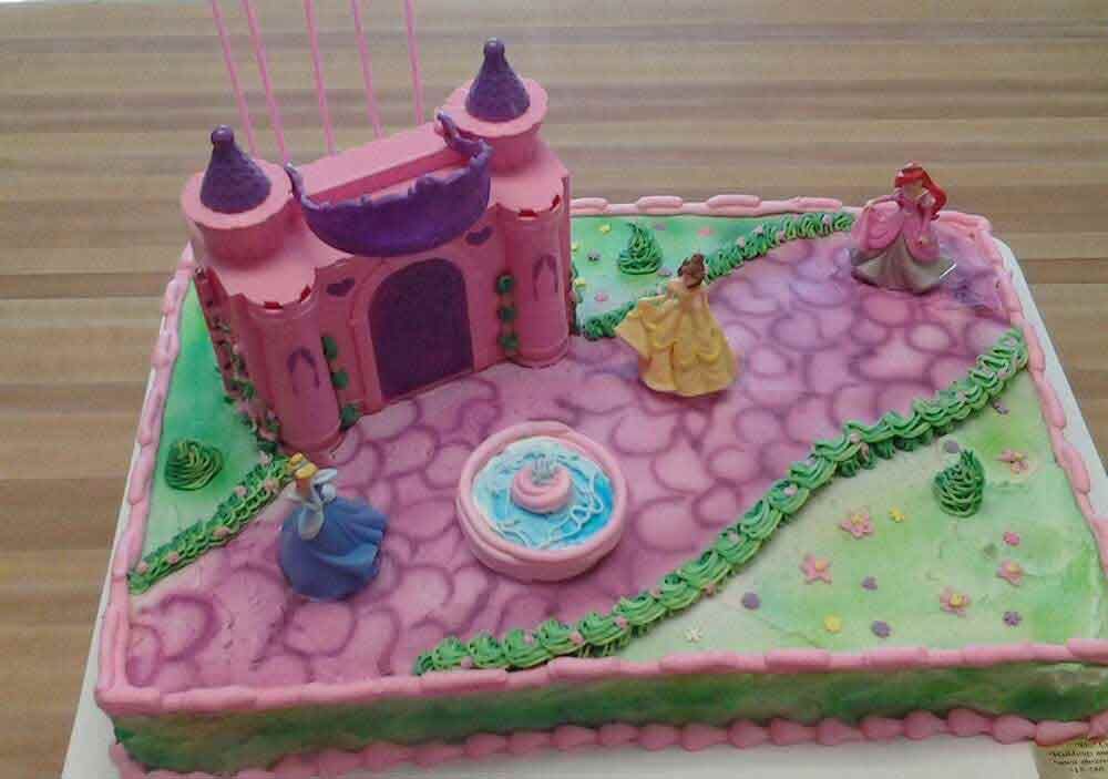 Princess-themed cake with pink castle, figurines, and green frosting accents on a table.