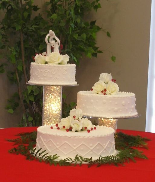 Wedding cakes, white frosting, tiered display, topped with roses and figurines, on a red table.