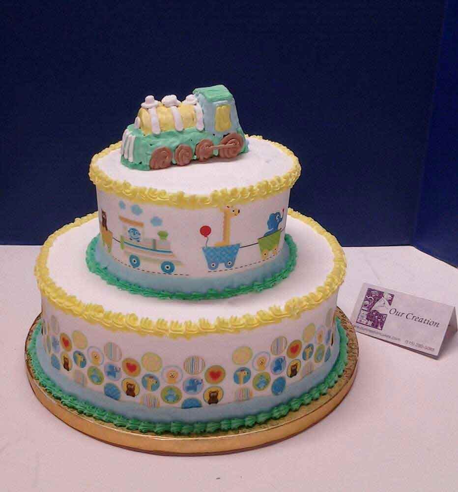 Two-tiered baby shower cake with train topper and colorful animal designs.