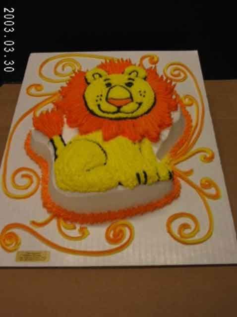 Lion-shaped birthday cake decorated with orange and yellow frosting, on a white rectangular base with orange swirls.