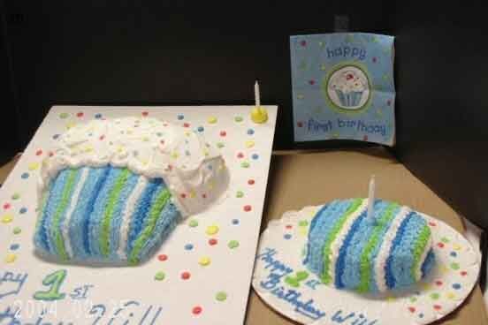 Two cupcake-shaped cakes and a card; one large, frosted, striped, and dotted; another small, striped with a candle; blue card says “Happy 1st Birthday”.