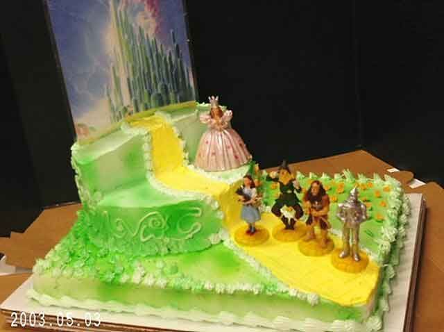 Wizard of Oz cake with yellow brick road, figures, and emerald city backdrop.