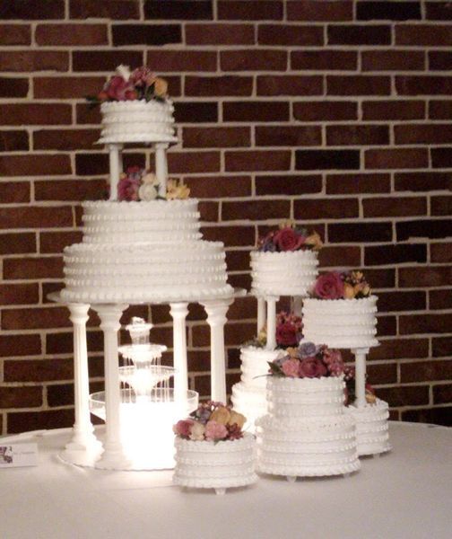 Wedding cakes on display; white tiered cakes with flower decorations on white pedestals against a brick wall.