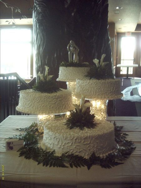 Four-tiered wedding cake with white frosting and floral decorations, displayed on a table.