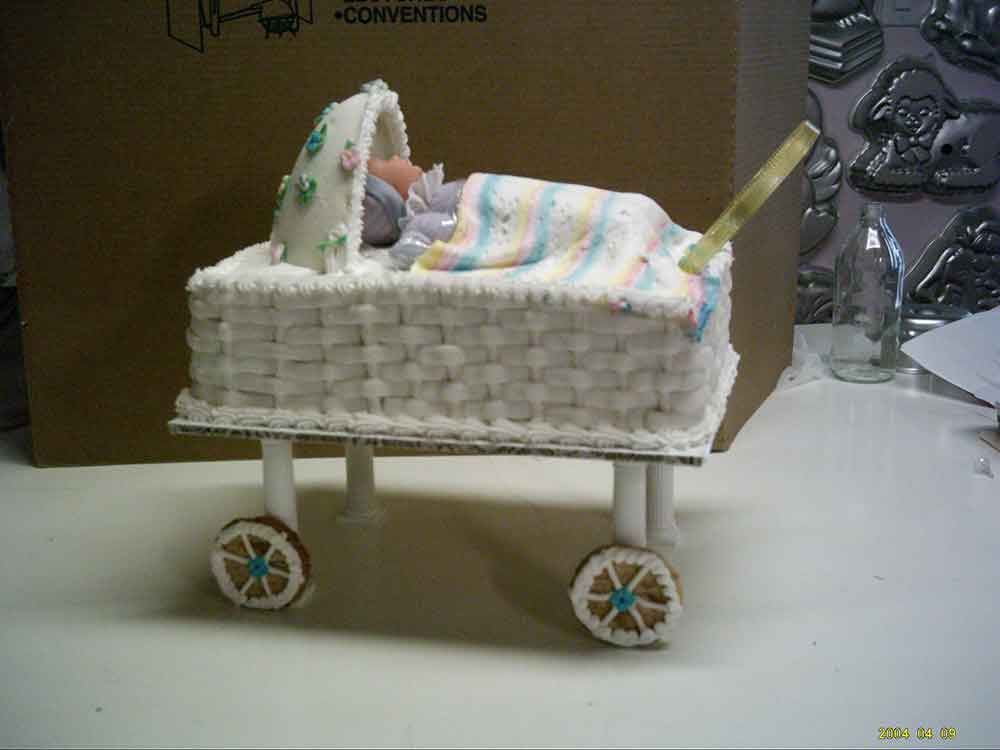 Gingerbread baby carriage cake with sleeping baby, white frosting, and wheels.